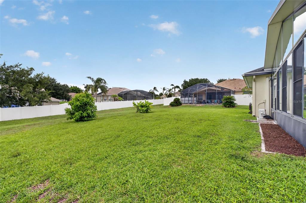 A grassy backyard features a white vinyl fence, two small shrubs, and a screened-in patio — 13529 VIA ROMA CIRCLE, CLERMONT, FL