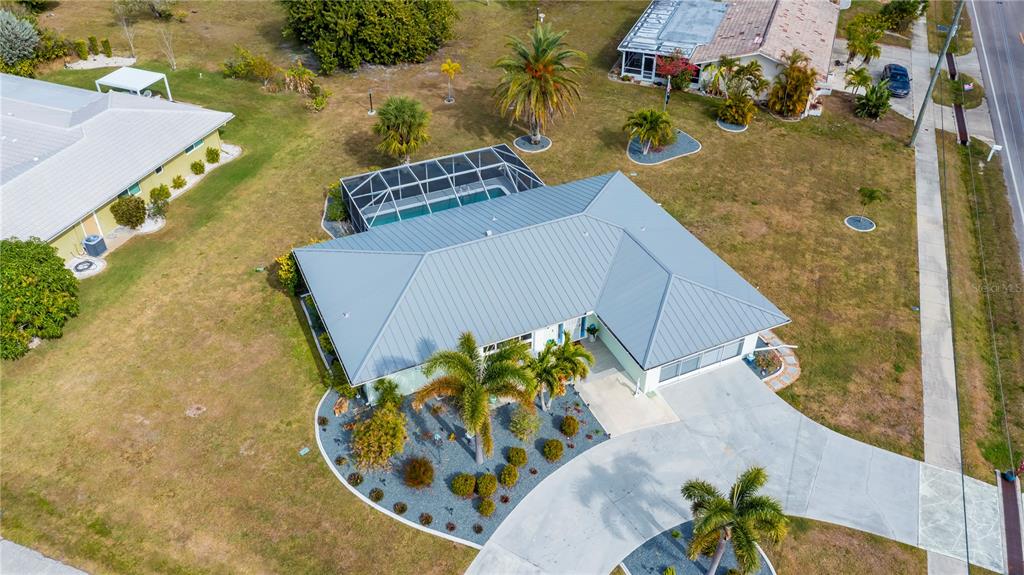 An aerial view shows a single-story house with a metal roof, pool cage, and driveway — 1354 AQUI ESTA DRIVE, PUNTA GORDA, FL