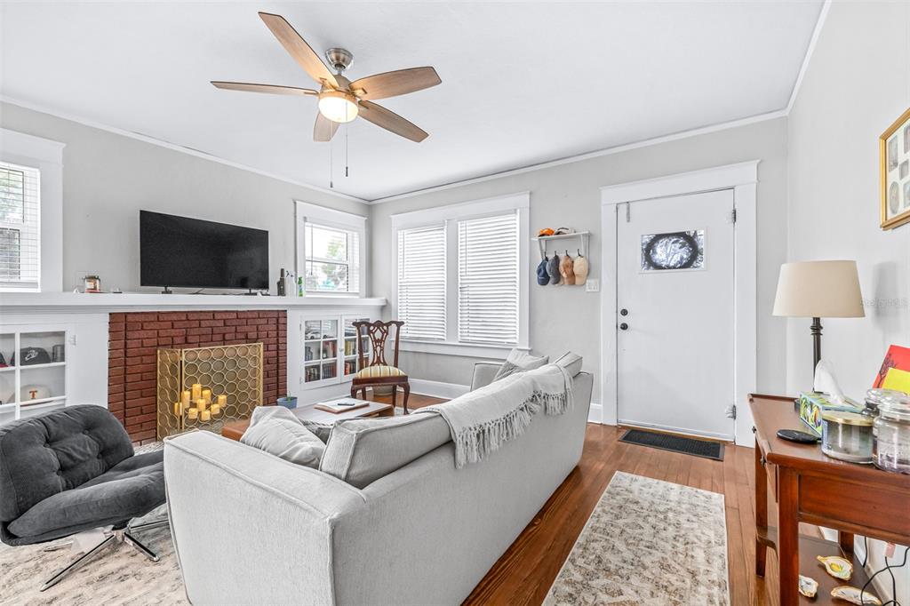 A living room features a brick fireplace, a gray sofa, a ceiling fan, and hardwood floors — 5503 N 9TH STREET, TAMPA, FL