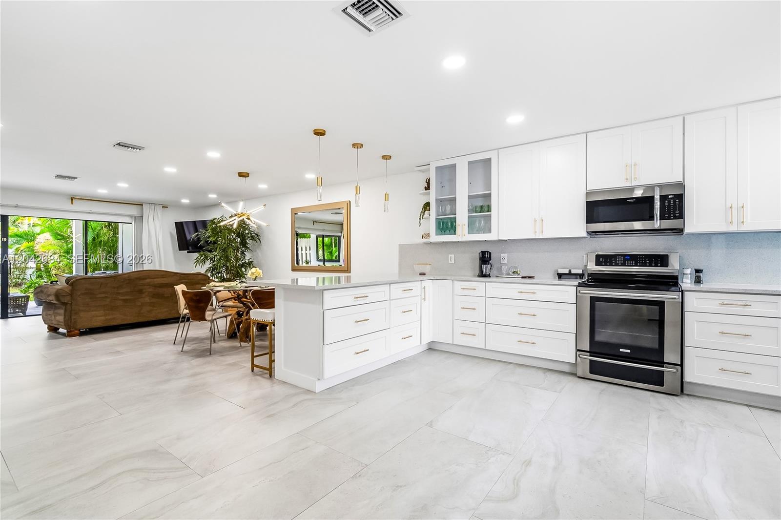 A modern, open-concept kitchen features white cabinetry, stainless steel appliances, and light-colored tile flooring — 1301 SW 10th Ave # 105, Delray Beach FL 33444, DELRAY BEACH, FL
