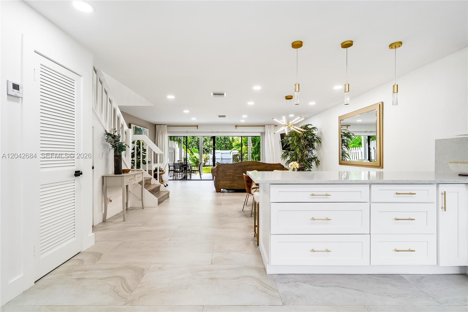 A bright, open-concept kitchen and living area features white cabinetry, gold hardware, and tile flooring — 1301 SW 10th Ave # 105, Delray Beach FL 33444, DELRAY BEACH, FL