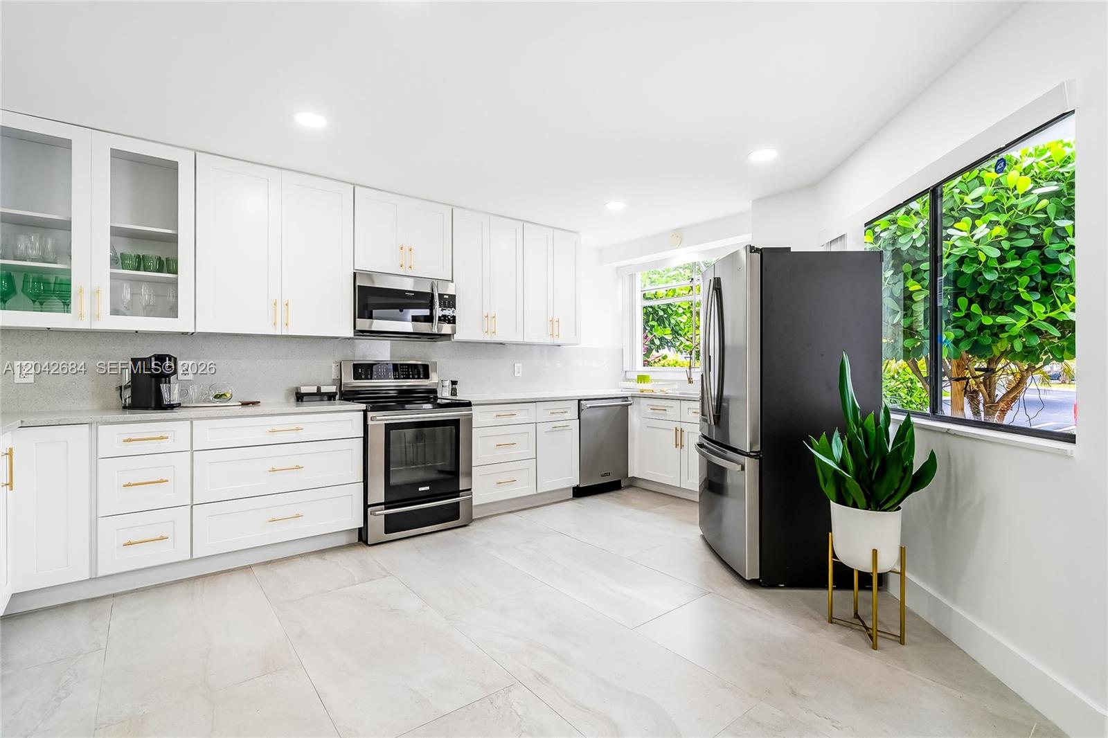 A modern kitchen features white cabinets, stainless steel appliances, and large windows with garden views — 1301 SW 10th Ave # 105, Delray Beach FL 33444, DELRAY BEACH, FL