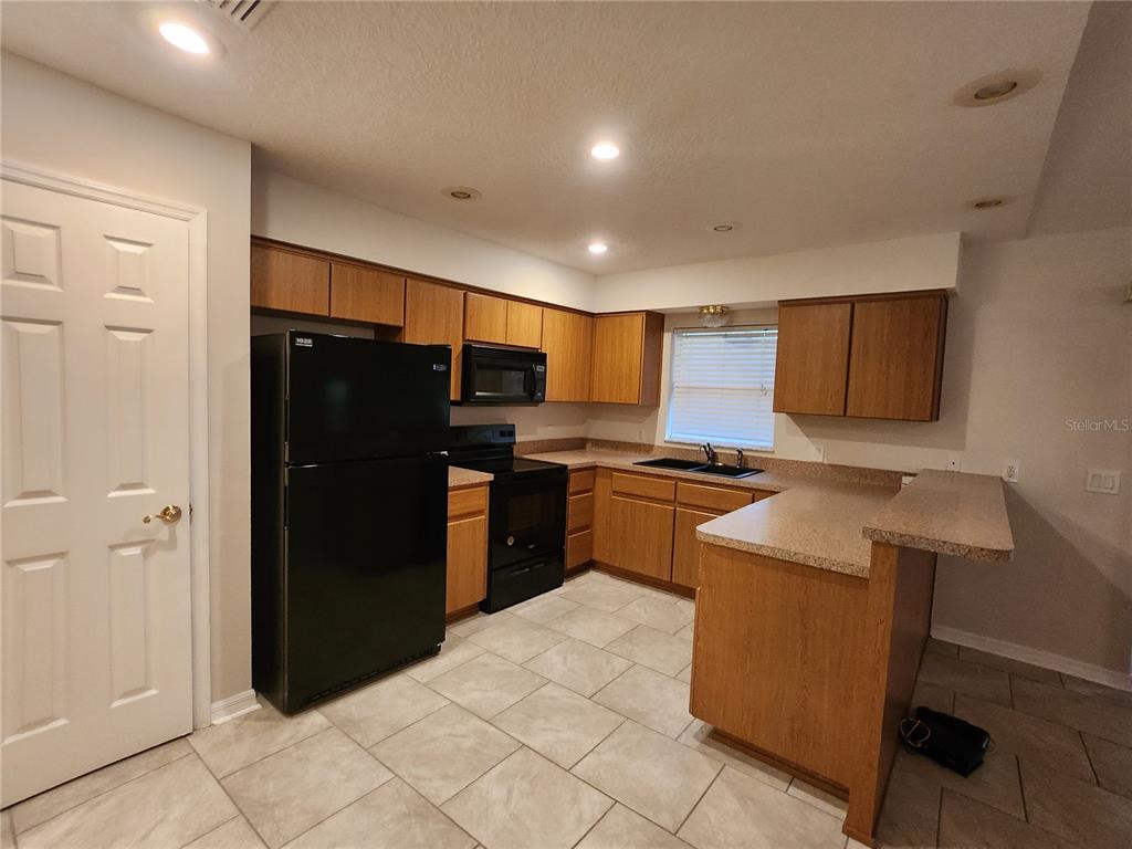 A kitchen features wood cabinets, black appliances, a breakfast bar, and light-colored tile flooring — 6521 E GRAYSON STREET, INVERNESS, FL