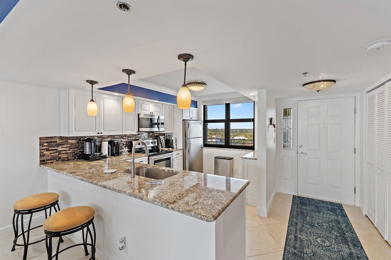 A kitchen with granite countertops, white cabinets, and a breakfast bar overlooks a scenic view — 840 Ocean Drive # 905, Juno Beach FL 33408, JUNO BEACH, FL