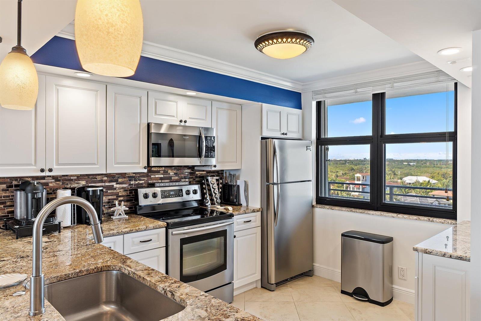 A kitchen features white cabinets, granite countertops, stainless steel appliances, and a window with views — 840 Ocean Drive # 905, Juno Beach FL 33408, JUNO BEACH, FL