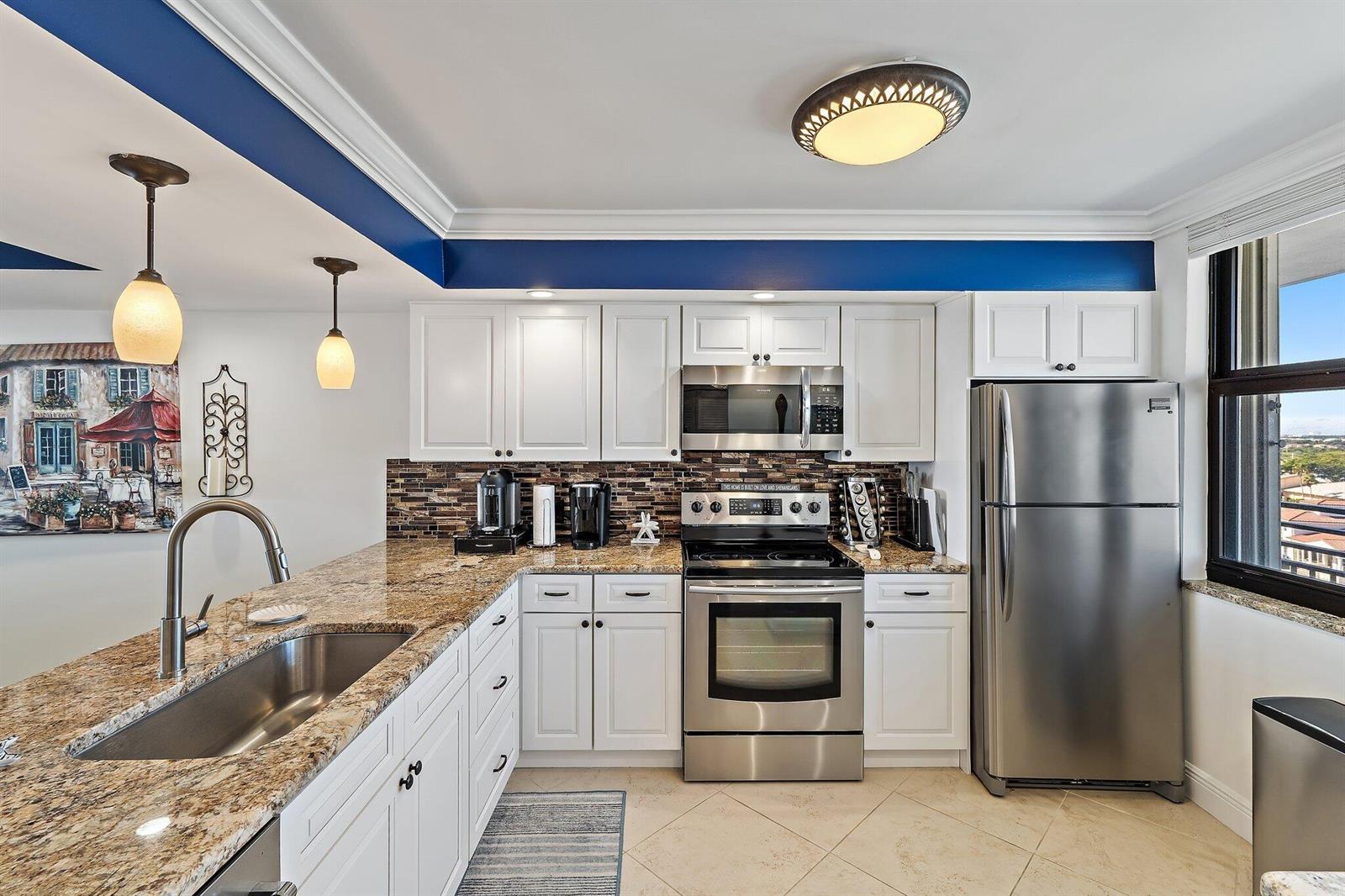 A kitchen features white cabinets, granite countertops, stainless steel appliances, and a blue accent wall — 840 Ocean Drive # 905, Juno Beach FL 33408, JUNO BEACH, FL