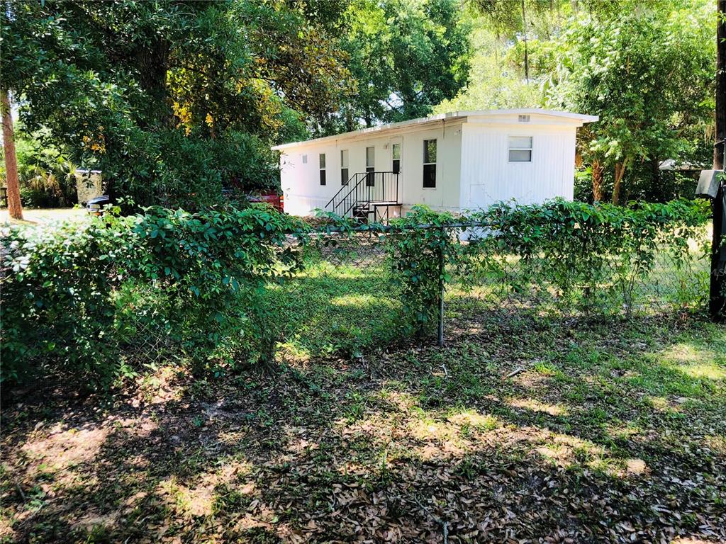 A white mobile home sits behind a chain-link fence surrounded by trees and foliage — 3545 SW 90TH STREET, OCALA, FL