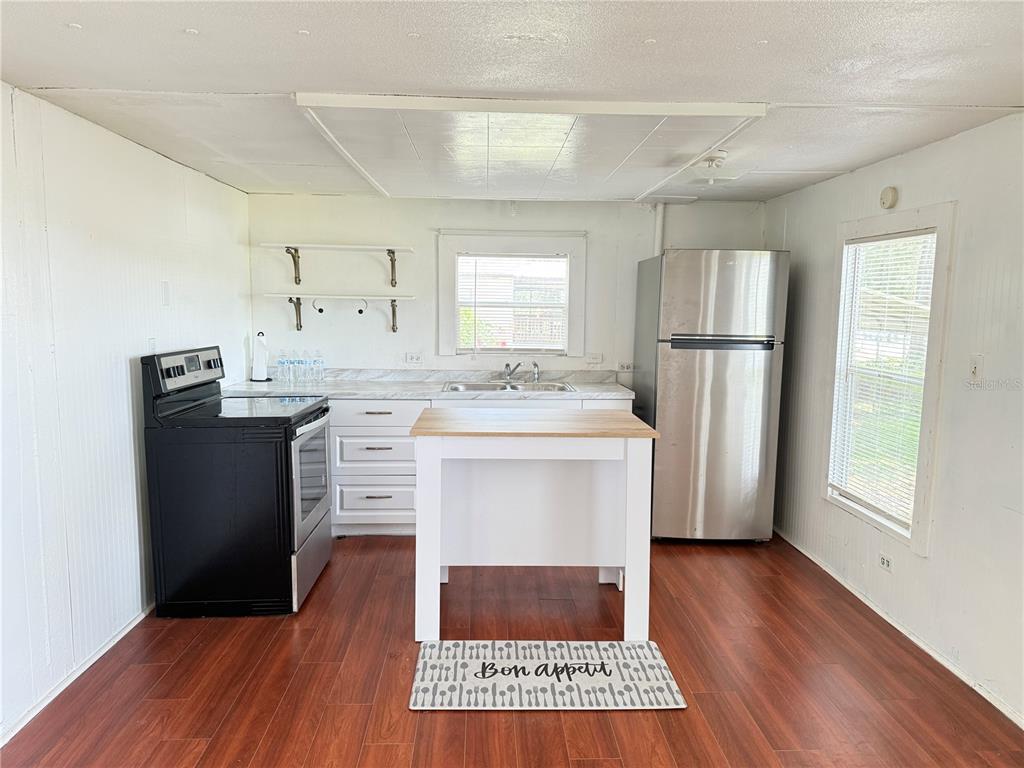 A kitchen with a black stove, stainless steel refrigerator, white island, and wood-look flooring — 3545 SW 90TH STREET, OCALA, FL