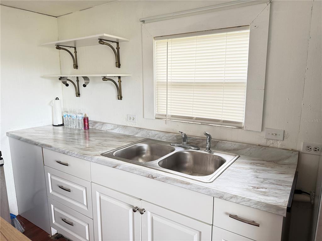 A kitchen features white cabinets, a marble-patterned countertop, a double-basin sink, and open wall shelving — 3545 SW 90TH STREET, OCALA, FL