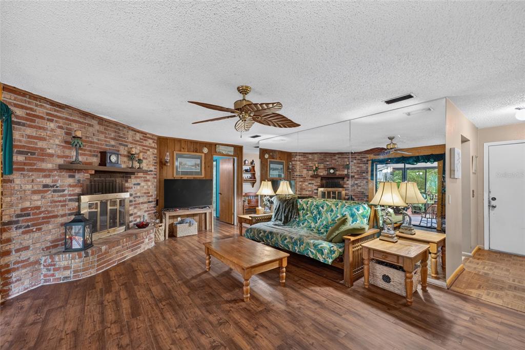A living room features a brick fireplace, wood-look flooring, a ceiling fan, and mirrored walls — 8204 SW 12TH PLACE, GAINESVILLE, FL
