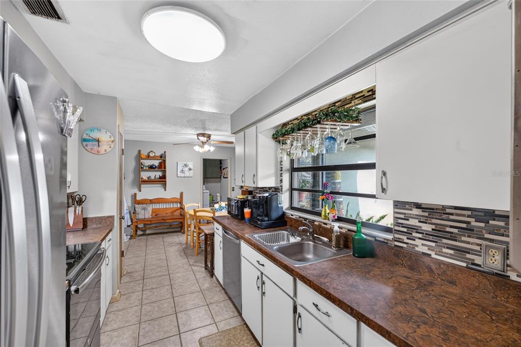 A kitchen with white cabinets, dark countertops, and a tile backsplash leads to a dining area — 8204 SW 12TH PLACE, GAINESVILLE, FL