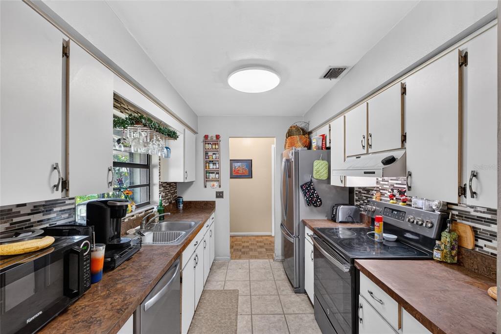 A galley kitchen features white cabinets, dark countertops, stainless steel appliances, and tiled flooring — 8204 SW 12TH PLACE, GAINESVILLE, FL