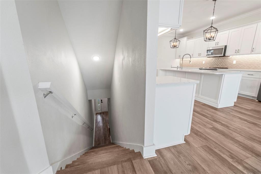 A view looking down a staircase toward a kitchen with white cabinets and wood flooring — 1299 SAVONA DRIVE NE, ST PETERSBURG, FL