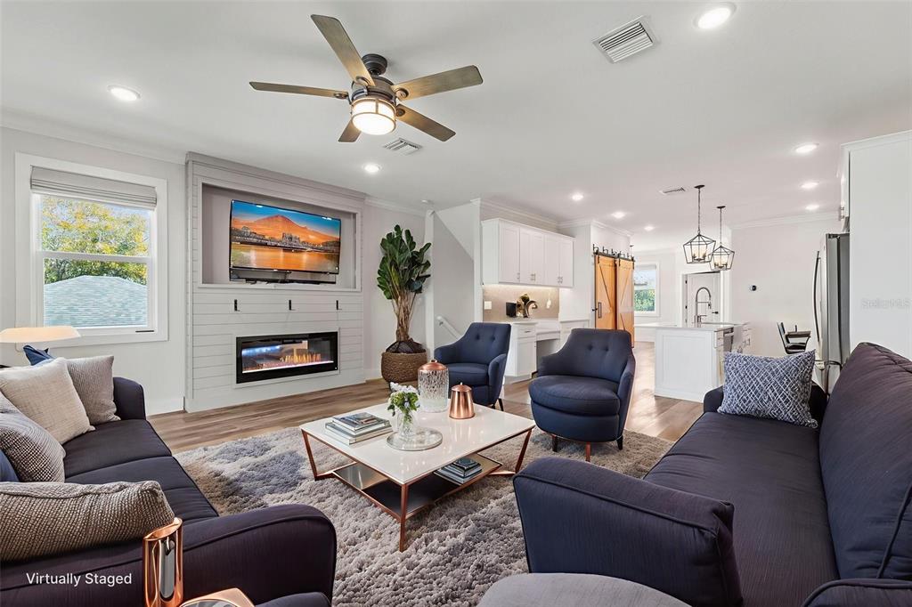 A living room features a fireplace, a television, navy seating, and an open kitchen area — 1299 SAVONA DRIVE NE, ST PETERSBURG, FL