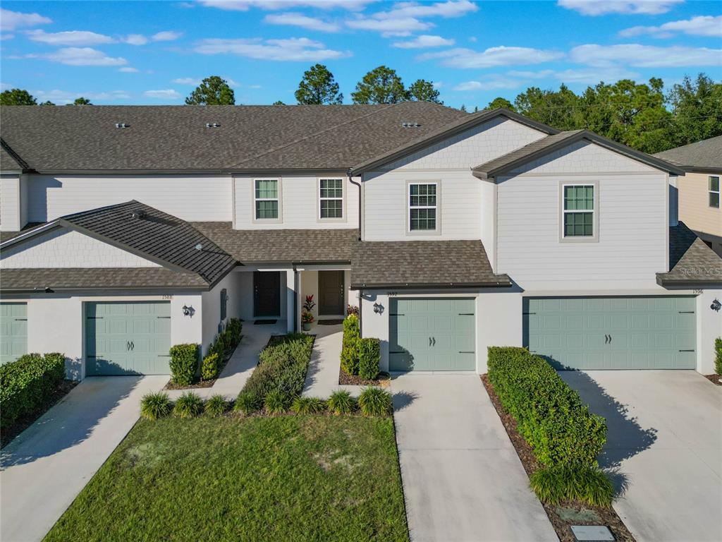 An exterior view of a multi-unit townhouse complex with light-colored siding and green garage doors — 1592 WYNFORD CIRCLE, TAVARES, FL