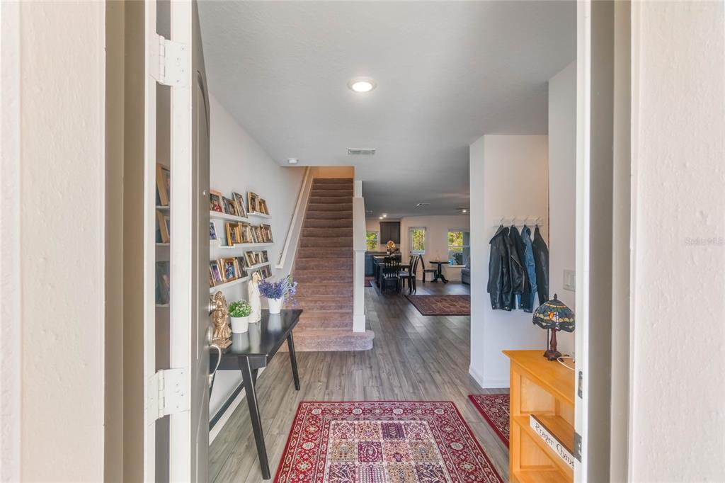 An entryway leads to a carpeted staircase, a hallway with wood-look flooring, and an open kitchen — 1592 WYNFORD CIRCLE, TAVARES, FL