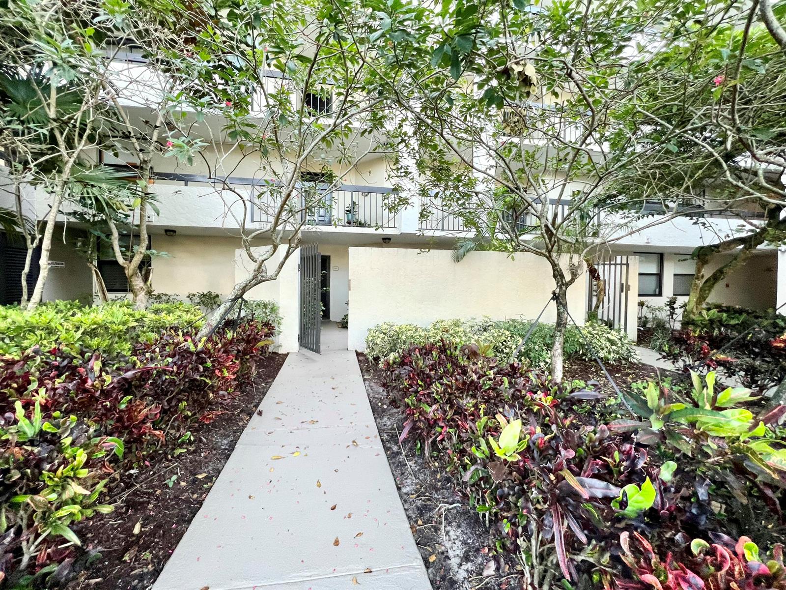 A concrete walkway leads to the entrance of a multi-story apartment building with landscaped gardens — 2025 Lavers Circle # D107, Delray Beach FL 33444, DELRAY BEACH, FL