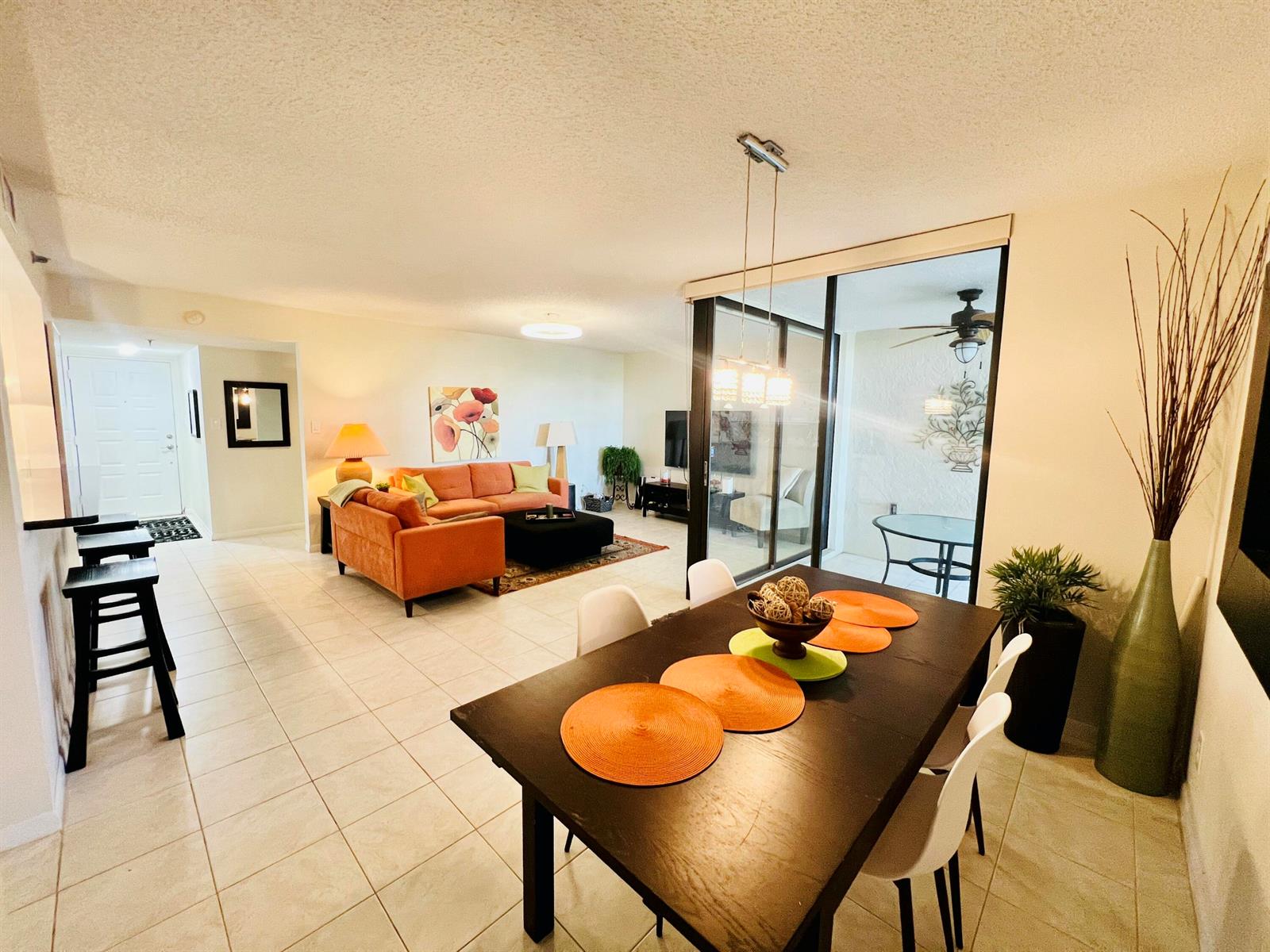 An open-concept living and dining area features tile flooring, an orange sofa, and sliding glass doors — 2025 Lavers Circle # D107, Delray Beach FL 33444, DELRAY BEACH, FL