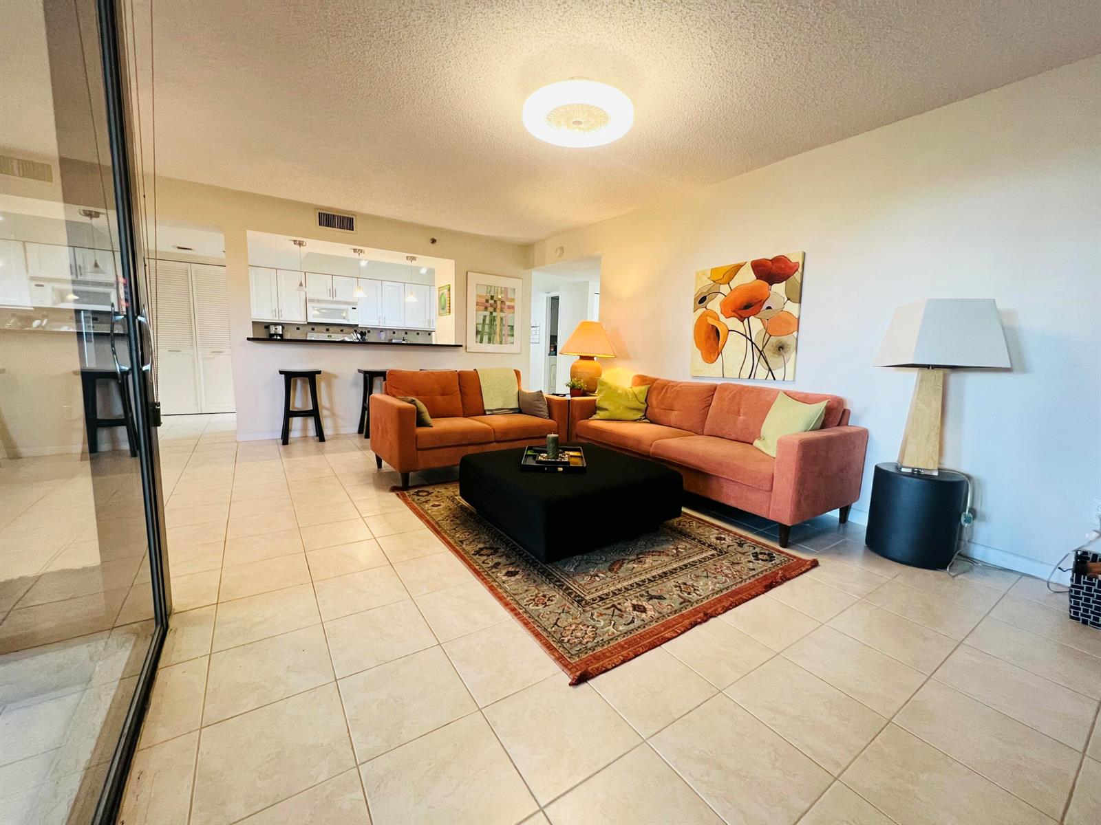 A living room with orange sofas, a black ottoman, and tile flooring near a kitchen — 2025 Lavers Circle # D107, Delray Beach FL 33444, DELRAY BEACH, FL