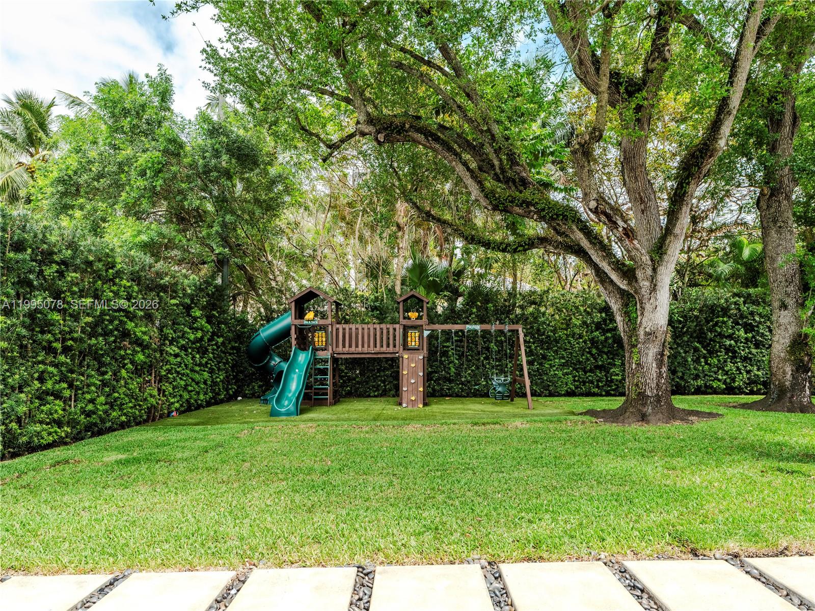 A wooden playground set with a slide and swings sits on a lawn near trees — 8525 SW 54th Ct, Miami FL 33143, MIAMI, FL