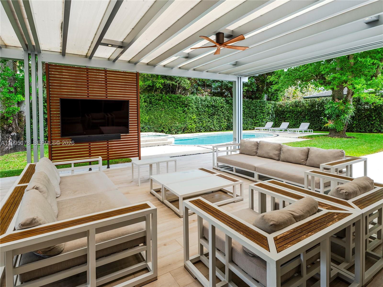 A covered outdoor patio features modern seating, a television on a wood-slat wall, and a pool — 8525 SW 54th Ct, Miami FL 33143, MIAMI, FL