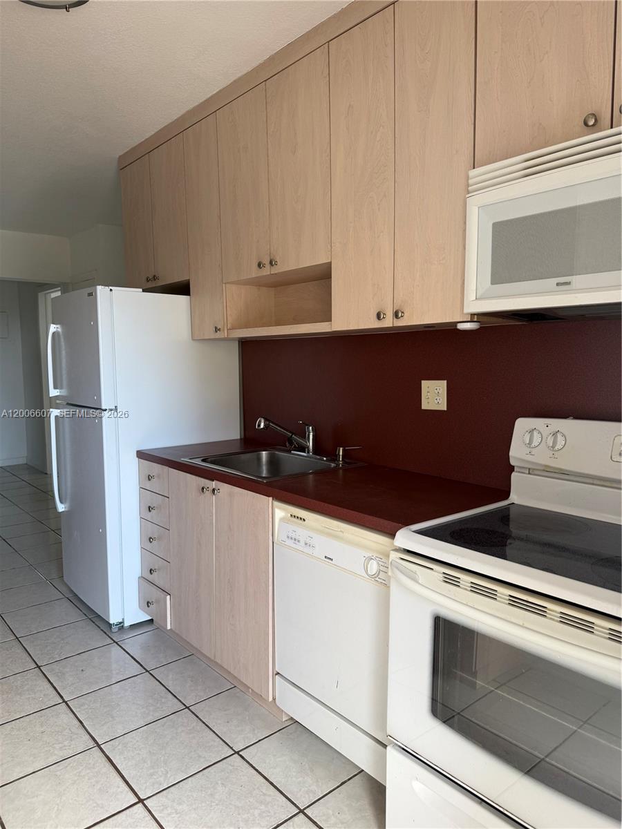 A kitchen features light wood cabinets, a dark countertop, white appliances, and tiled flooring — 2600 S Ocean Dr # S306, Hollywood FL 33019, HOLLYWOOD, FL