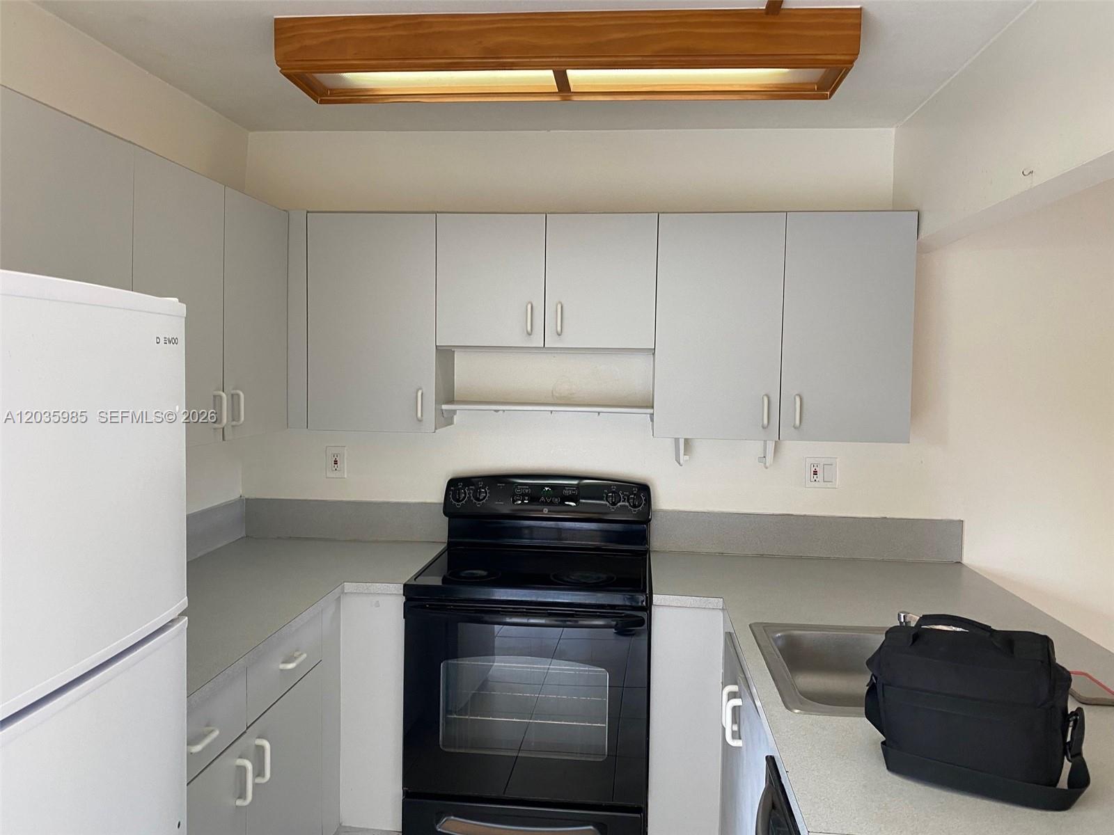 A kitchen features light gray cabinets, a black stove, a white refrigerator, and laminate countertops — 15695 SW 82nd Cir Ln # 5, Miami FL 33193, MIAMI, FL