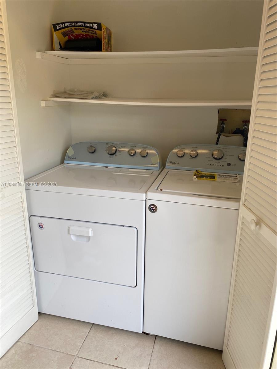 A laundry closet contains a white washer and dryer beneath two open storage shelves — 15695 SW 82nd Cir Ln # 5, Miami FL 33193, MIAMI, FL