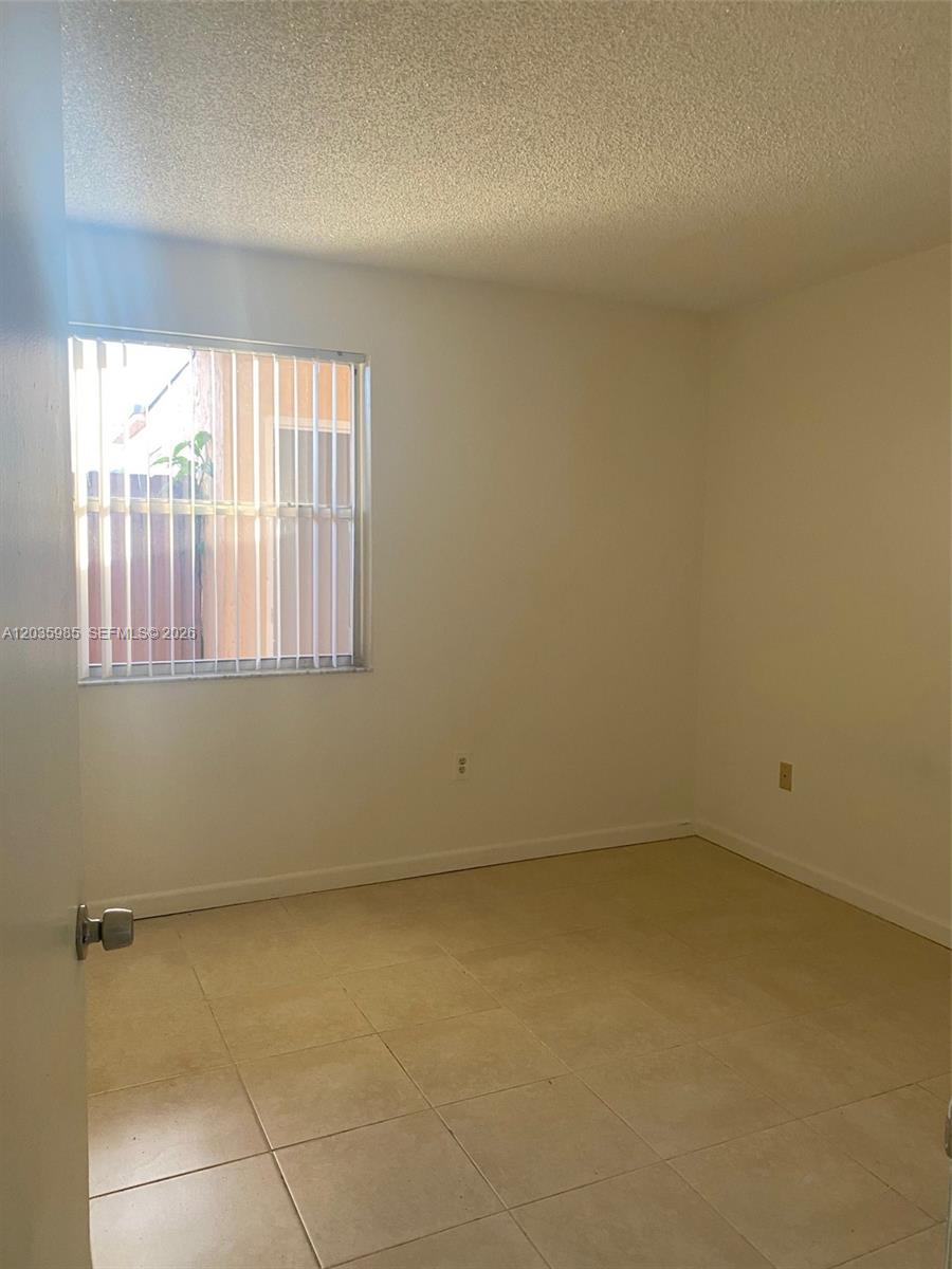 An empty bedroom features beige tile flooring, white walls, and a window with vertical blinds — 15695 SW 82nd Cir Ln # 5, Miami FL 33193, MIAMI, FL