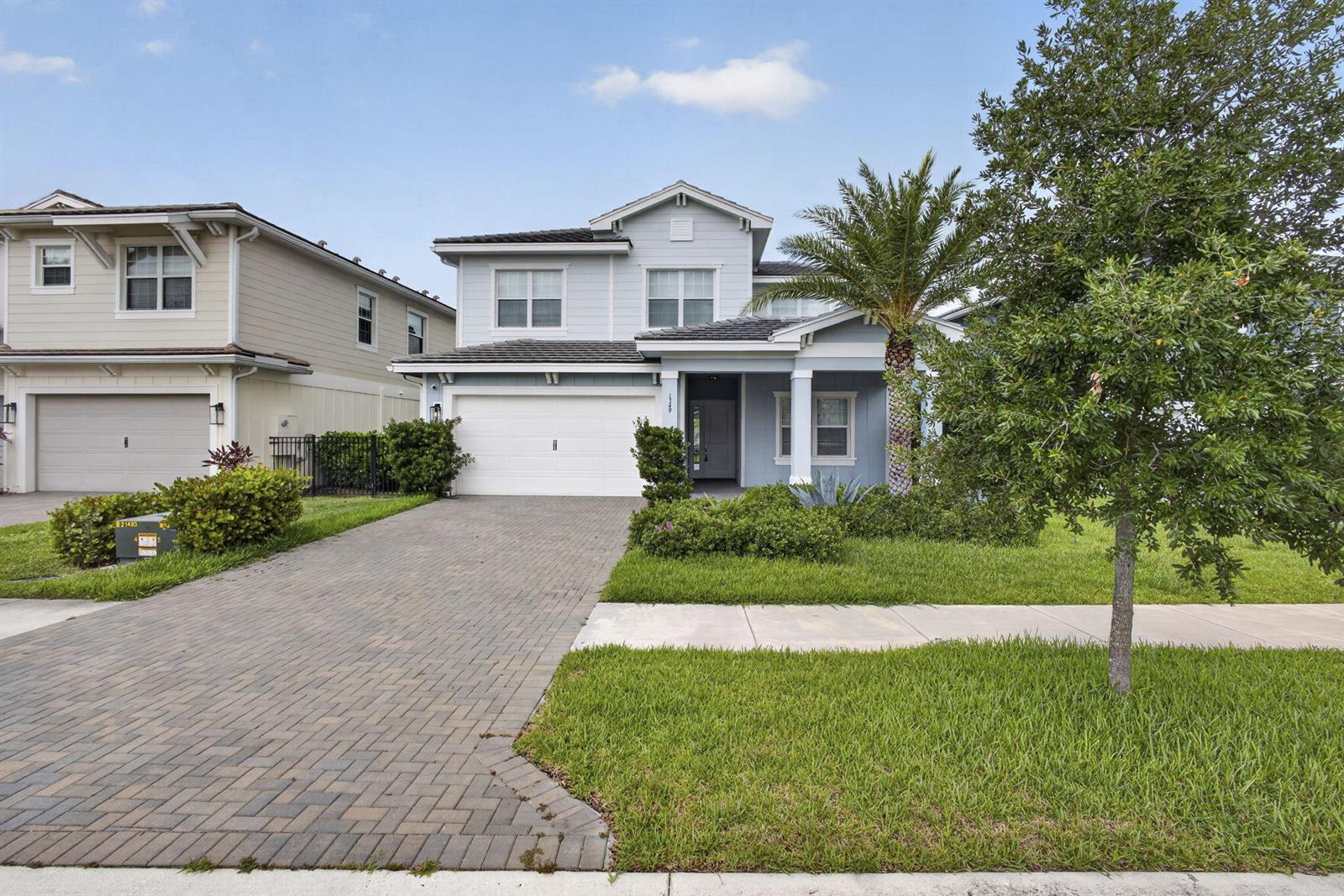 A two-story light blue house with a brick driveway and a palm tree in front — LOXAHATCHEE, FL
