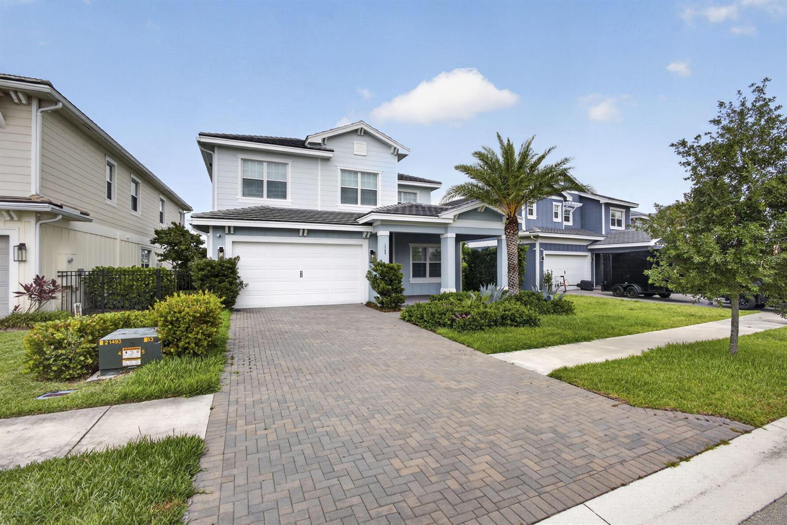 A two-story light blue house with a paved driveway and a palm tree in front — LOXAHATCHEE, FL