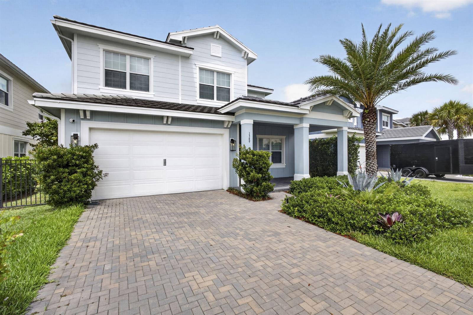 A two-story light blue house features a white garage door and a paved driveway — LOXAHATCHEE, FL