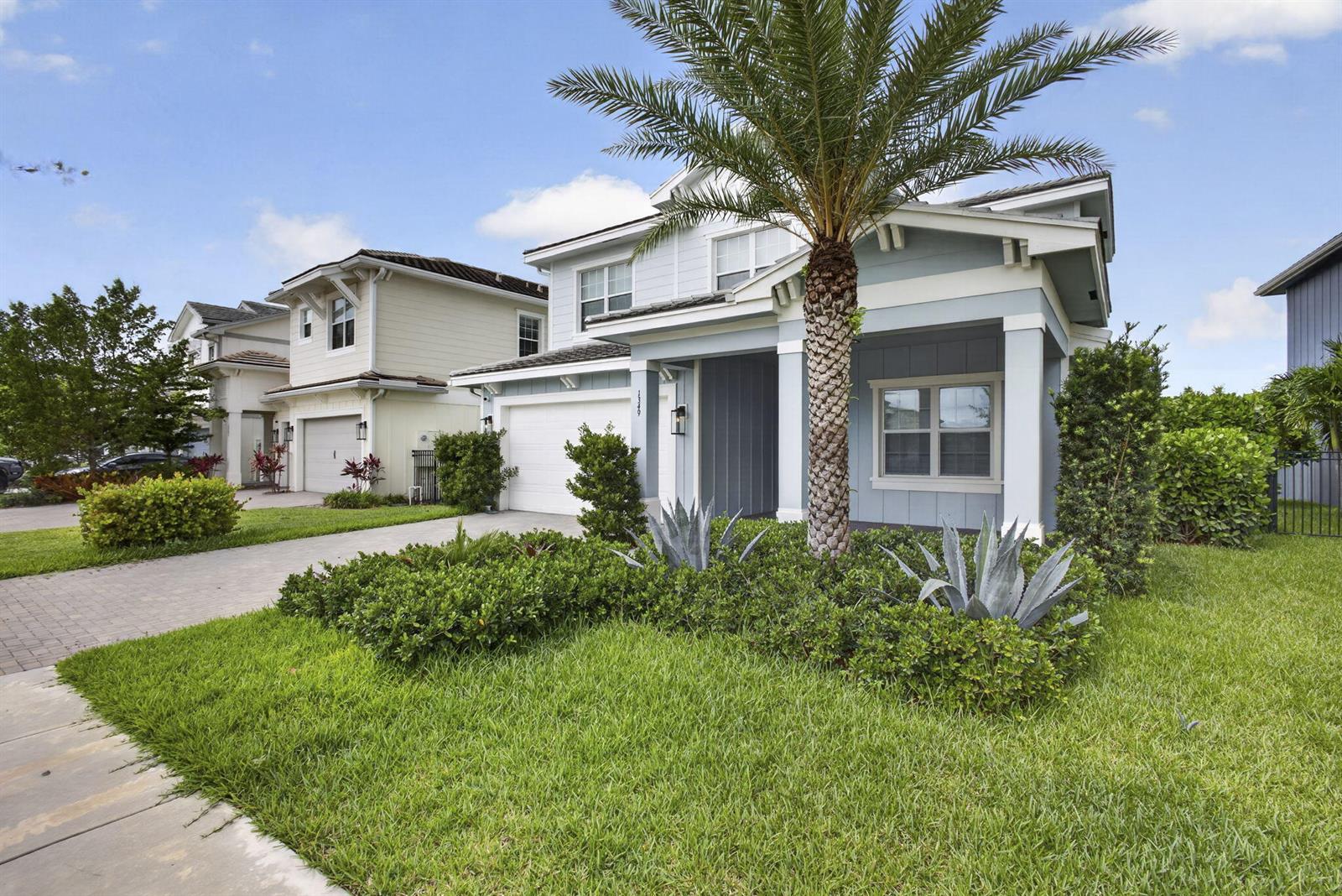 A two-story blue house features a palm tree in the front yard and a driveway — LOXAHATCHEE, FL