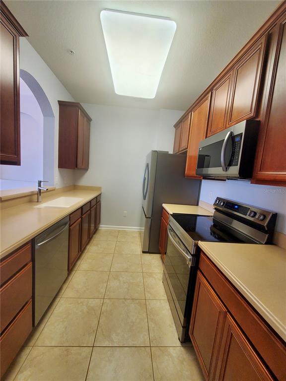 A galley kitchen features wood cabinets, stainless steel appliances, and light-colored countertops — 3338 ROBERT TRENT JONES DRIVE UNIT 40104, ORLANDO, FL