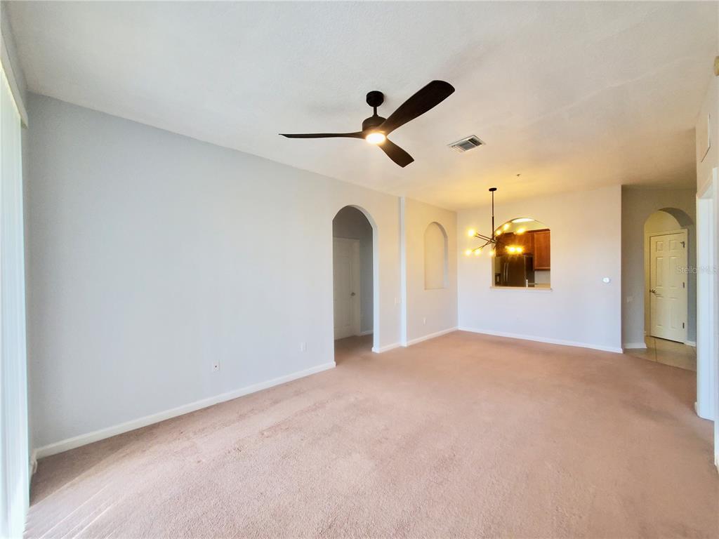 An empty living room features beige carpet, a ceiling fan, and arched doorways — 3338 ROBERT TRENT JONES DRIVE UNIT 40104, ORLANDO, FL