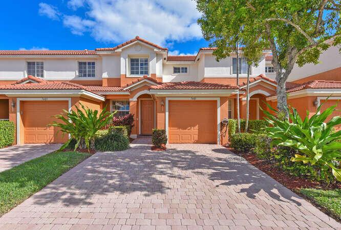 An exterior view of a two-story townhouse with orange stucco walls and a paved driveway — 7401 Sarentino Lane # 211, Boynton Beach FL 33437, BOYNTON BEACH, FL