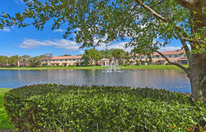 A pond with a fountain sits in front of multi-story residential buildings and trees — 7401 Sarentino Lane # 211, Boynton Beach FL 33437, BOYNTON BEACH, FL