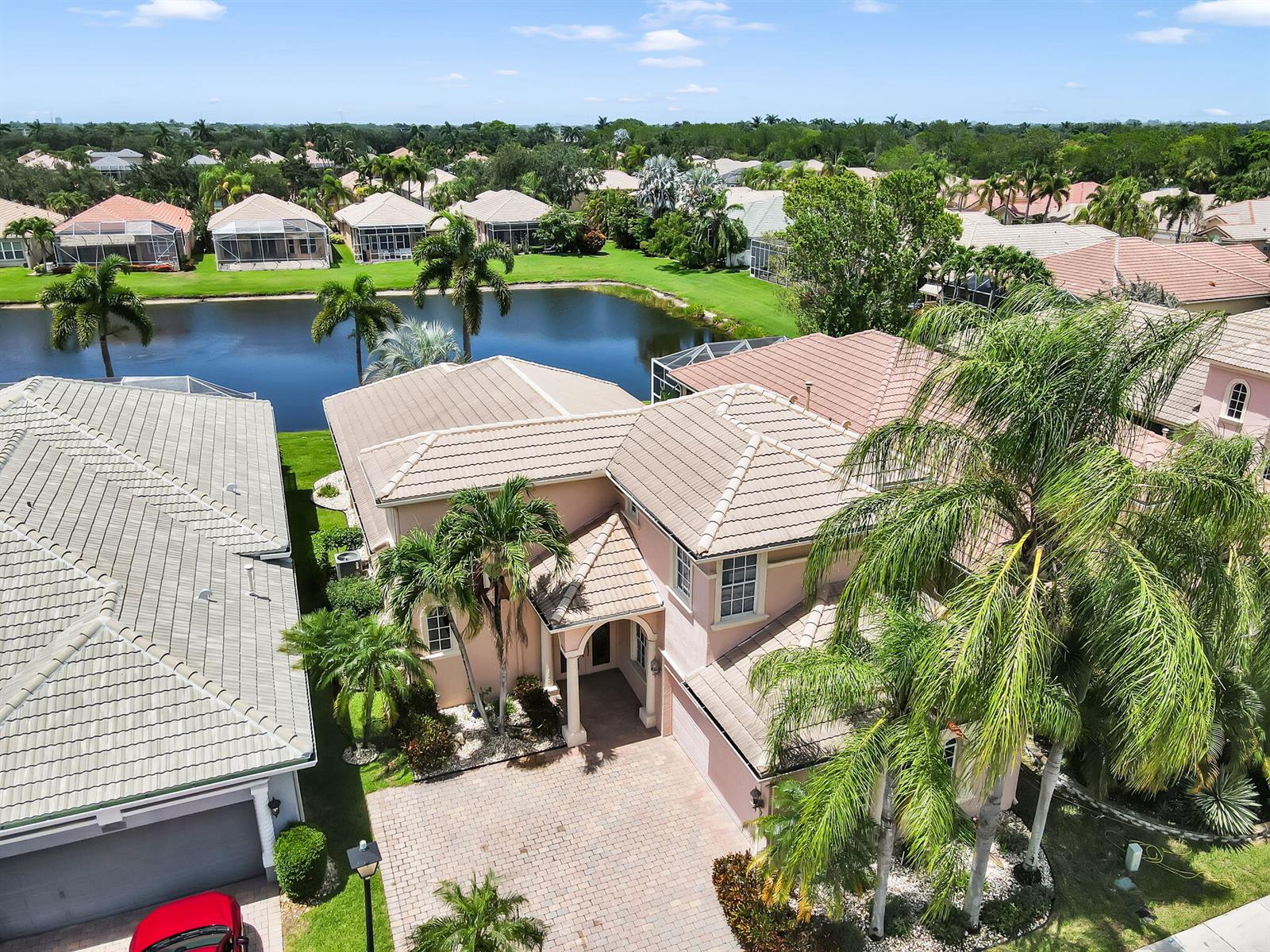 An aerial view shows a pink two-story house with a tiled roof and a lake — 7049 Veneto Drive, Boynton Beach FL 33437, BOYNTON BEACH, FL