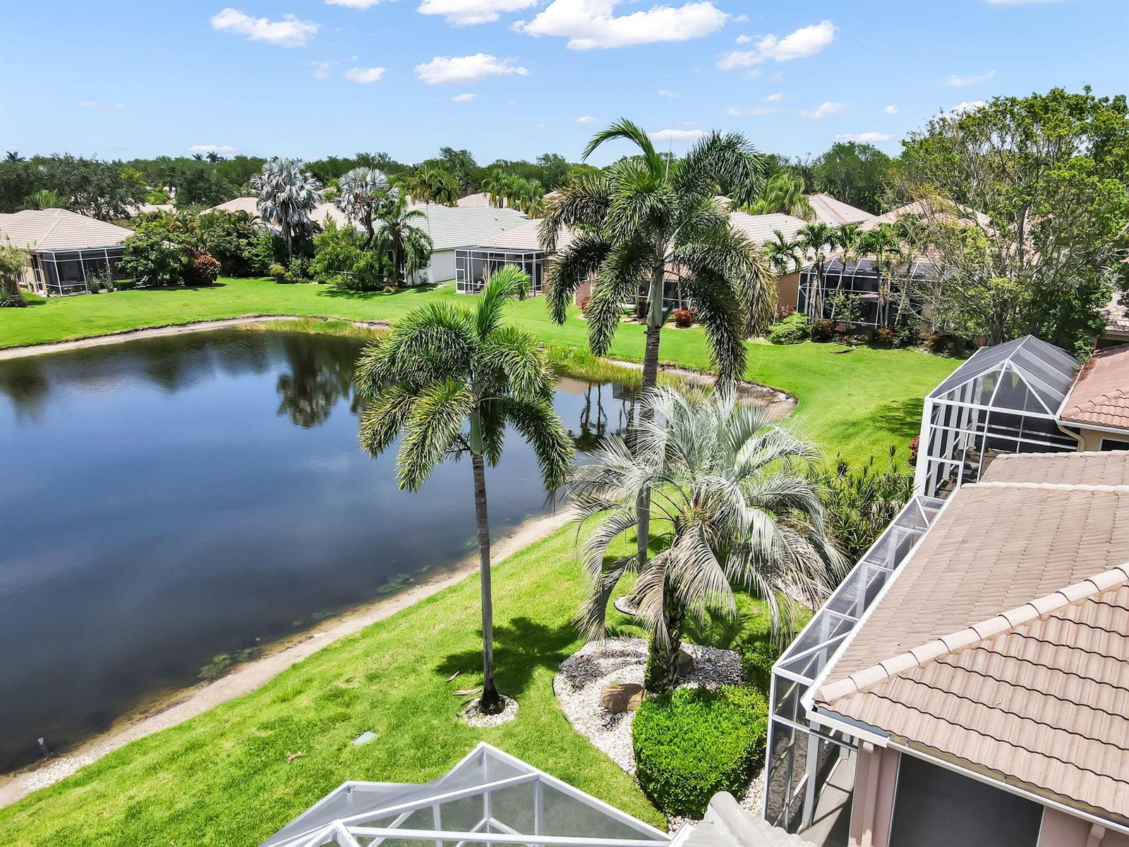 An elevated view of a backyard with a pond, palm trees, and screened-in lanais — 7049 Veneto Drive, Boynton Beach FL 33437, BOYNTON BEACH, FL