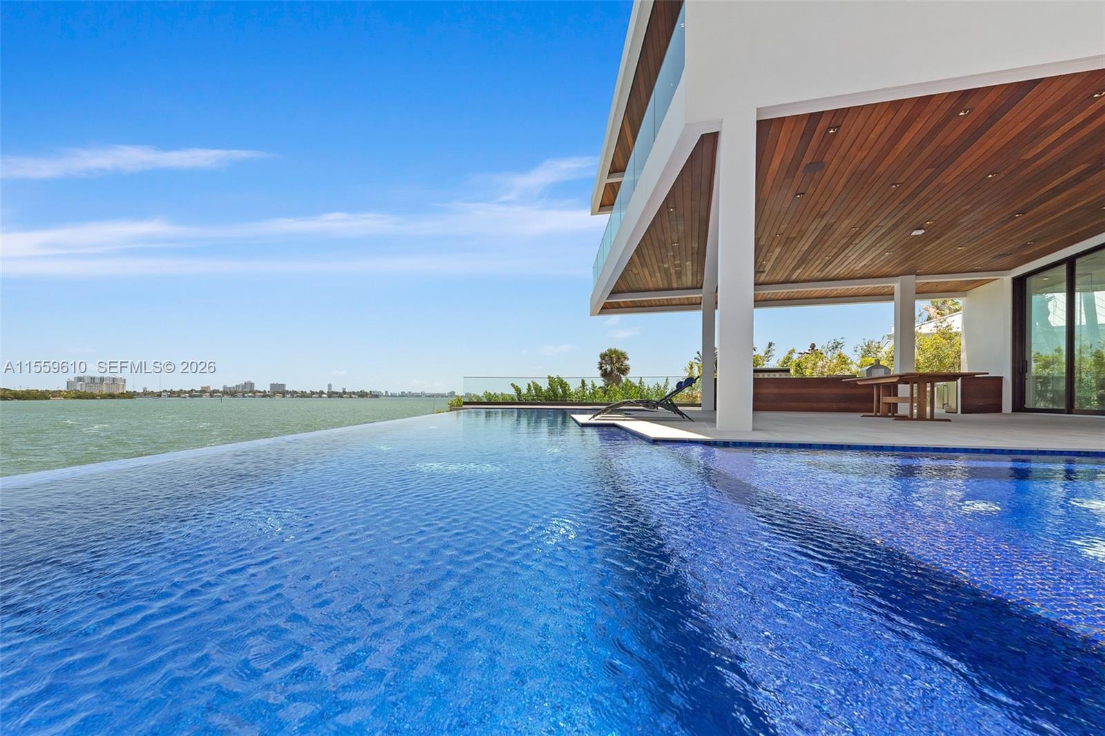 An infinity pool overlooks a bay from a modern home with a wood-paneled patio ceiling — 1133 Belle Meade Island Dr, Miami FL 33138, MIAMI, FL