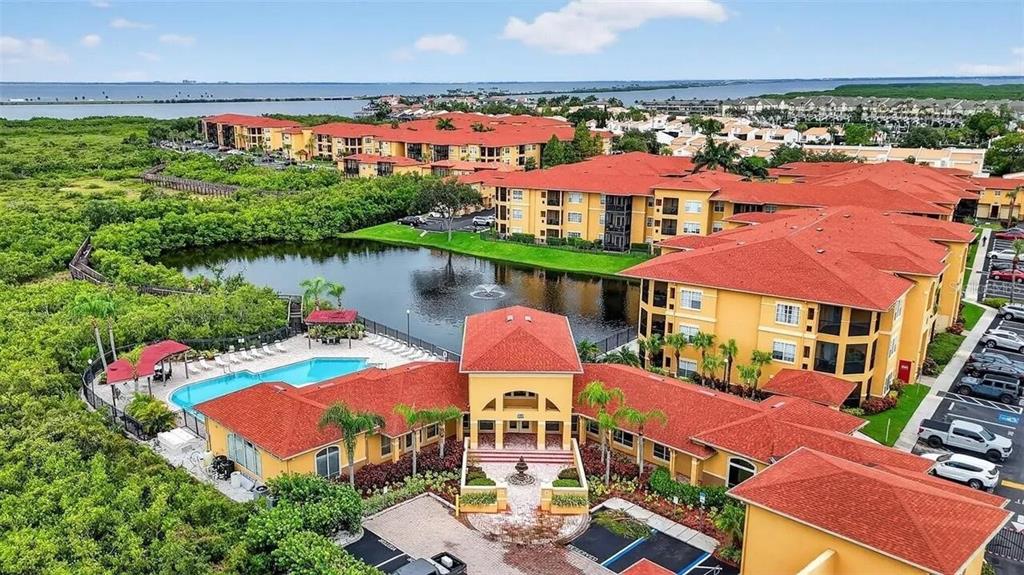 An aerial view shows a multi-story apartment complex with red roofs, a pool, and pond — 4333 BAYSIDE VILLAGE DRIVE UNIT 322, TAMPA, FL