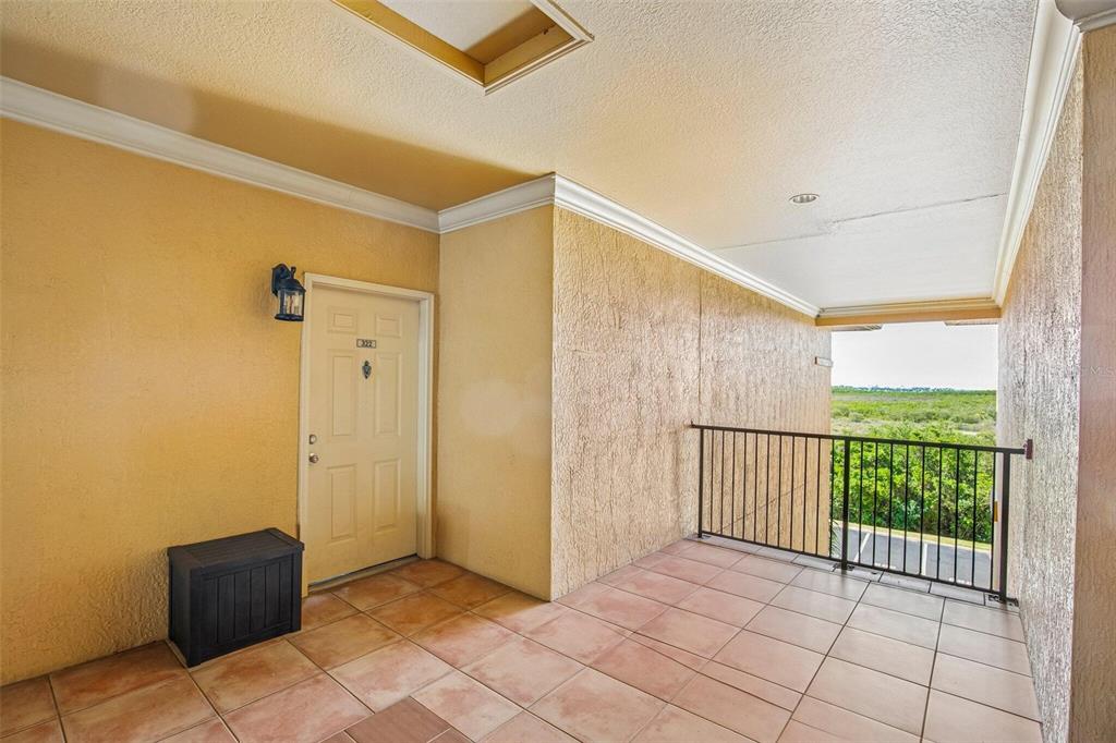 A covered outdoor balcony features tiled flooring, a beige door, and a black metal railing — 4333 BAYSIDE VILLAGE DRIVE UNIT 322, TAMPA, FL