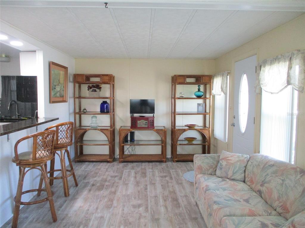 A living room features rattan shelving, a floral sofa, bar stools, and wood-look flooring — 34542 SWEETPEA LANE, ZEPHYRHILLS, FL