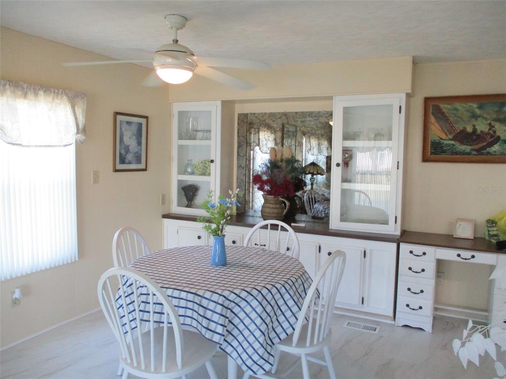 A dining room features a round table, white chairs, and built-in cabinetry with glass doors — 34542 SWEETPEA LANE, ZEPHYRHILLS, FL