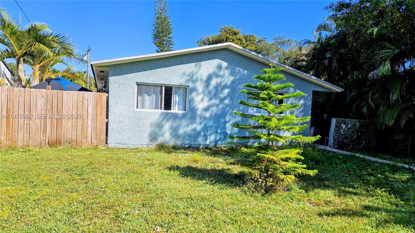 A light blue, single-story house exterior features a front yard with a small evergreen tree — 2411 Thomas St, Hollywood FL 33020, HOLLYWOOD, FL