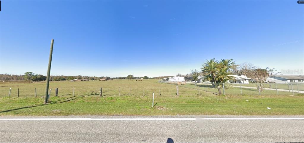 A wide, grassy field is bordered by a wire fence and a paved road — OLD POLK CITY RD, POLK CITY, FL