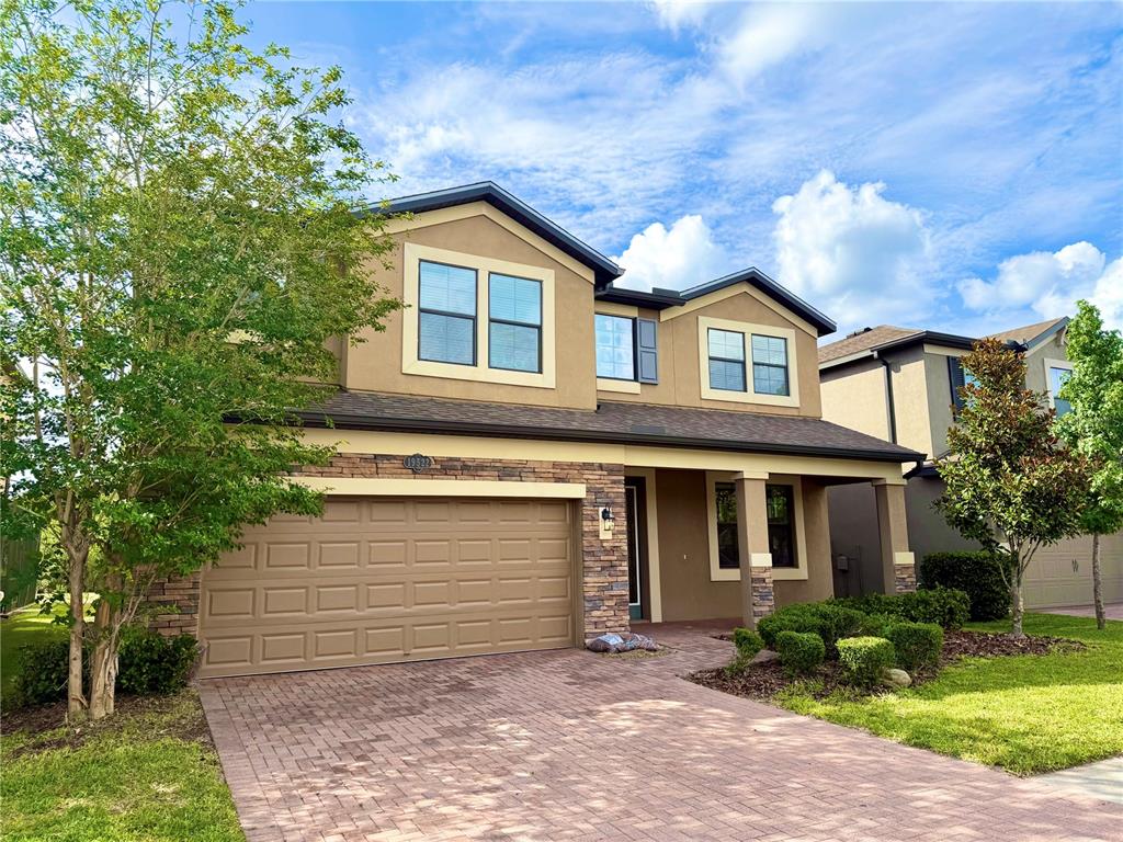 A two-story suburban house features a tan stucco exterior, stone accents, and a paved driveway — 19522 WHISPERING BROOK DRIVE, TAMPA, FL