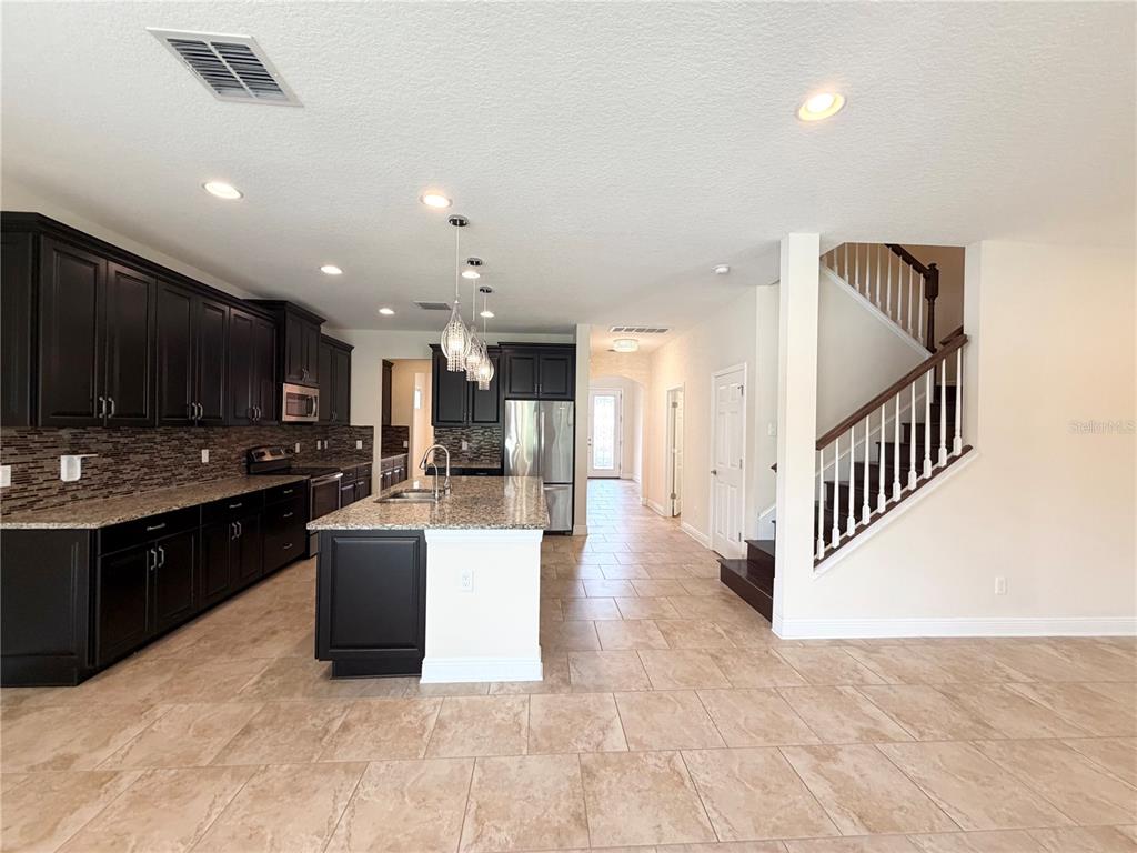 A kitchen with dark cabinets, granite countertops, and an island next to a staircase — 19522 WHISPERING BROOK DRIVE, TAMPA, FL