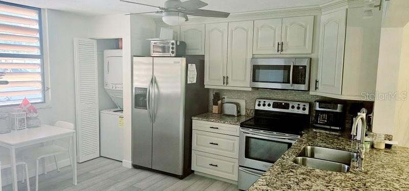A kitchen features white cabinetry, stainless steel appliances, granite countertops, and a laundry closet — 132 WILD PALM DRIVE UNIT 132, BRADENTON, FL
