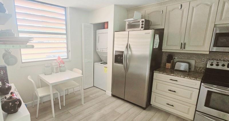 A kitchen features white cabinets, stainless steel appliances, a small dining table, and laundry closet — 132 WILD PALM DRIVE UNIT 132, BRADENTON, FL
